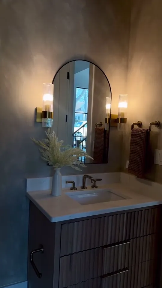 Still from the project reel: a finished powder room with an arched mirror and brass sconces.